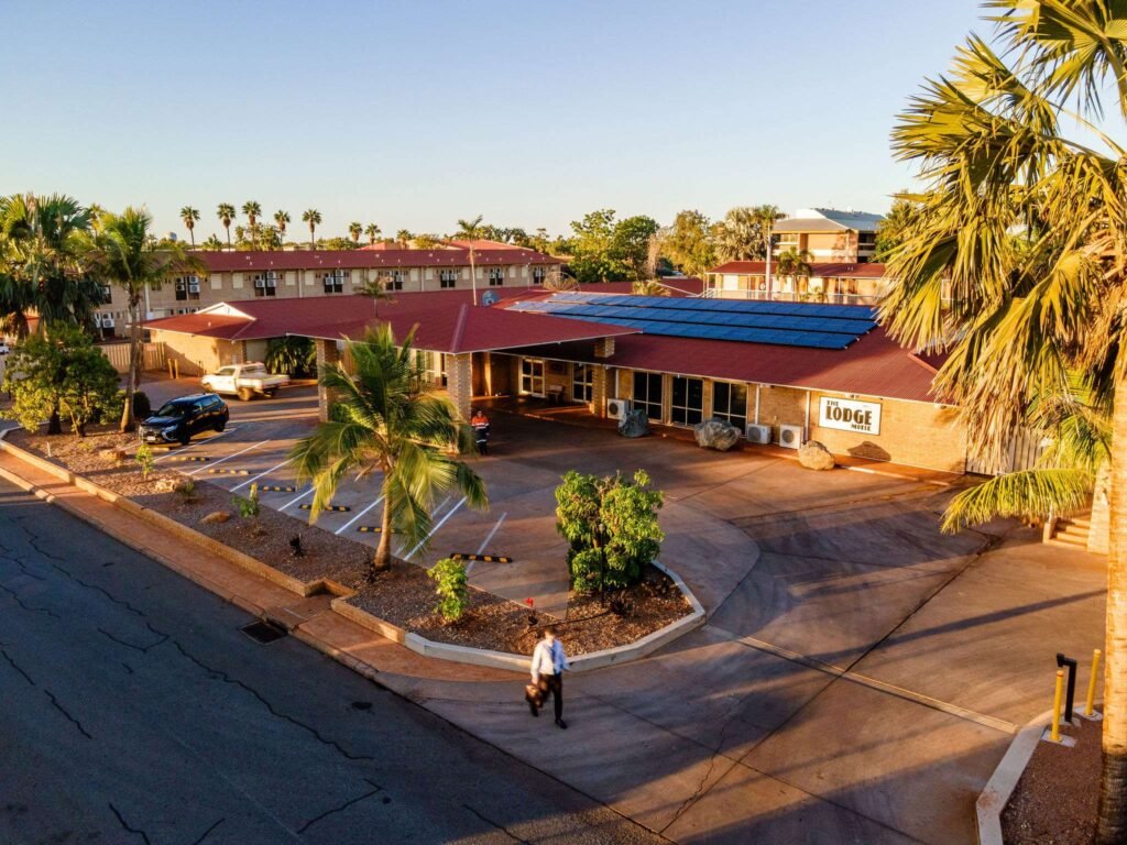 Aerial view of a small motel with a red roof and solar panels in a Pilbara town at sunrise, owner walking across the car park