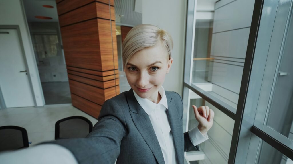 Young professional in a grey suit taking a selfie in a modern office, the early-career first home buyer weighing HECS debt and borrowing power