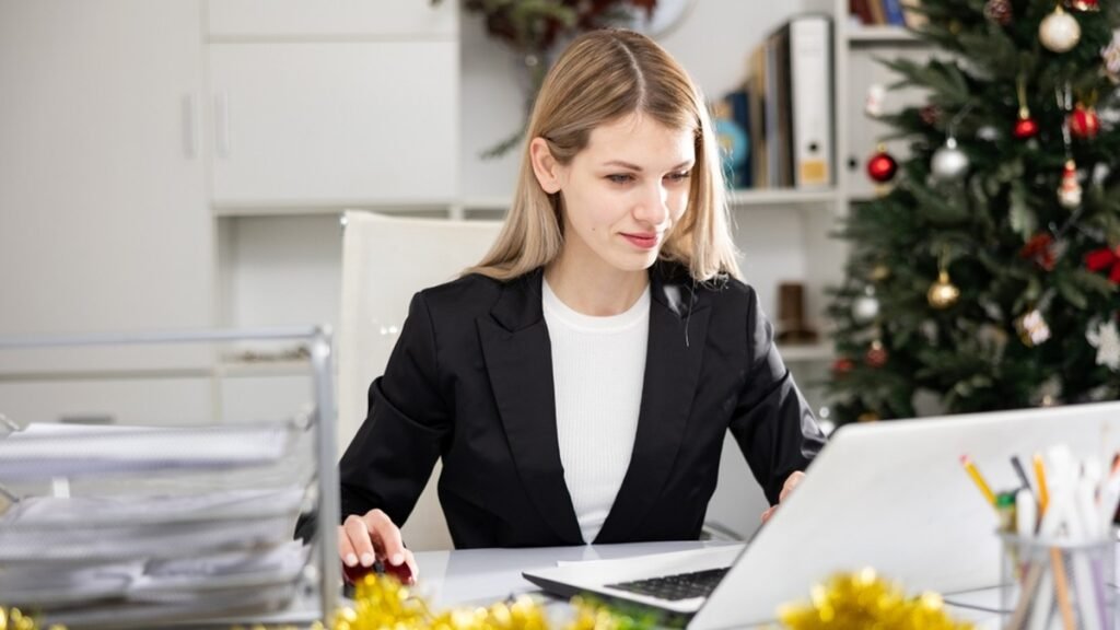 Business owner at her laptop sorting her finances before Christmas, with a decorated tree behind her